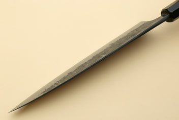 Gyuto knife side view with white steel blade and dark bolster, pointed tip.