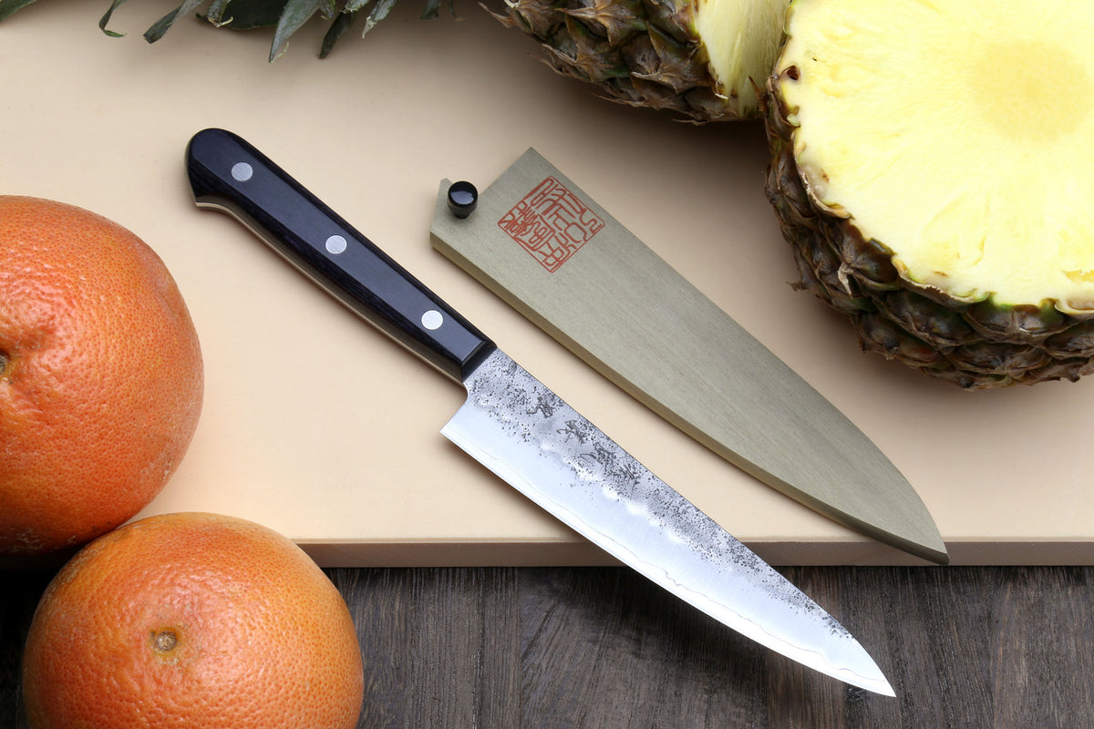 Petty utility knife with dark handle and speckled silver blade, beside wooden sheath