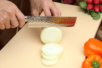 Nakiri knife with hammered Damascus blade, dark handle; chopping onion on cutting board