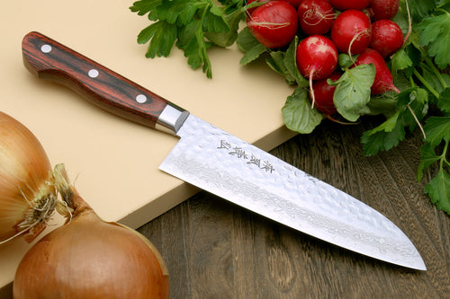 A Yoshihiro VG-10 16 Layer Hammered Damascus Stainless Steel Santoku Chef knife with a mahogany handle, displayed alongside fresh produce such as radishes and onions.